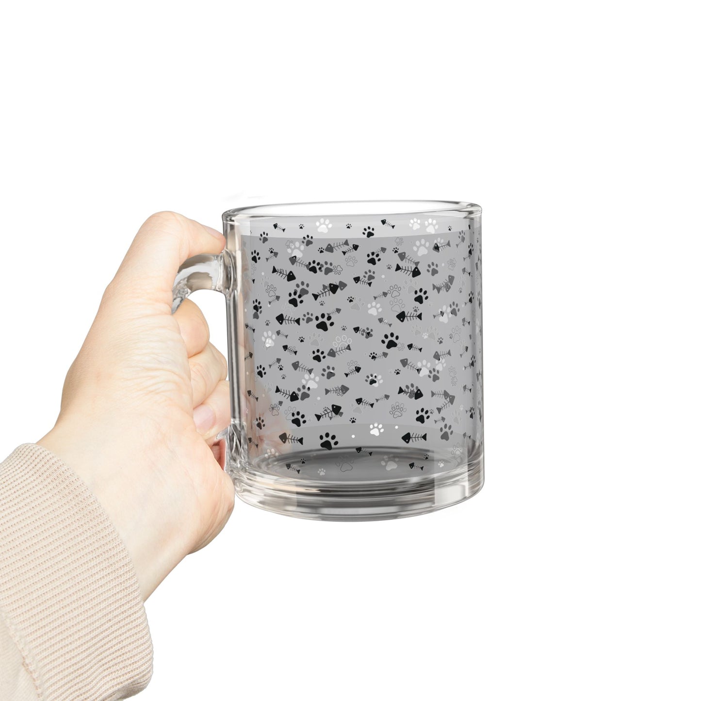 A hand holding a clear glass mug with paw prints and fishbones all over print pattern.