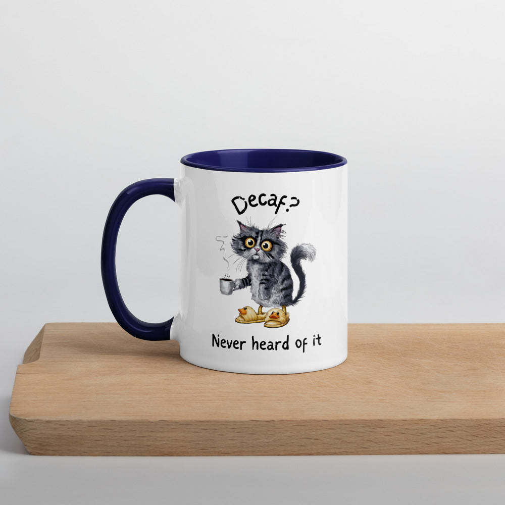 A white and dark blue mug featuring an exhausted looking cat wearing yellow slippers with duck faces on them. The cat is holding a steaming mug of coffee. The text on the mug reads "Decaf? Never Heard of It."