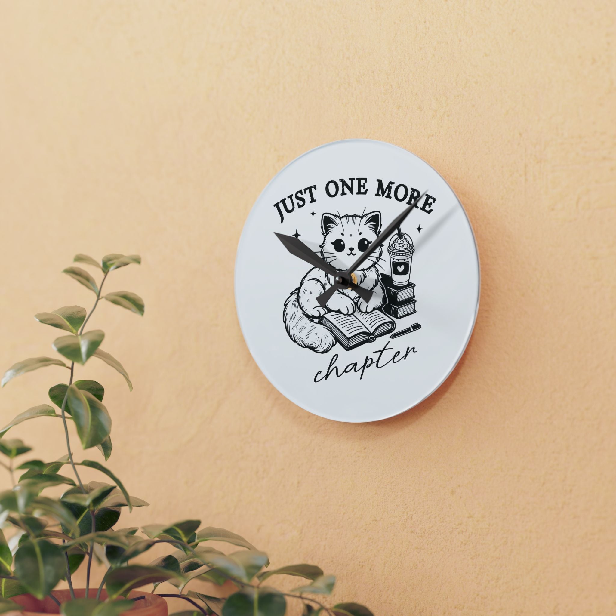 Line art graphic on the "Just One More Chapter" Acrylic Wall Clock depicting a cat reading an open book beside a book stack topped with a beverage. The words "just one more" are above, and "chapter" in script is below.