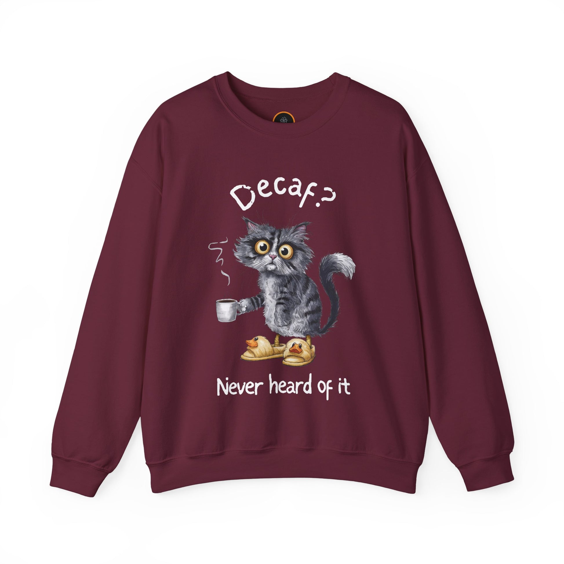 A sweatshirt featuring an exhausted-looking cat wearing yellow slippers with duck faces on them. The cat is holding a steaming mug of coffee. The text on the sweatshirt reads "Decaf? Never Heard of It."