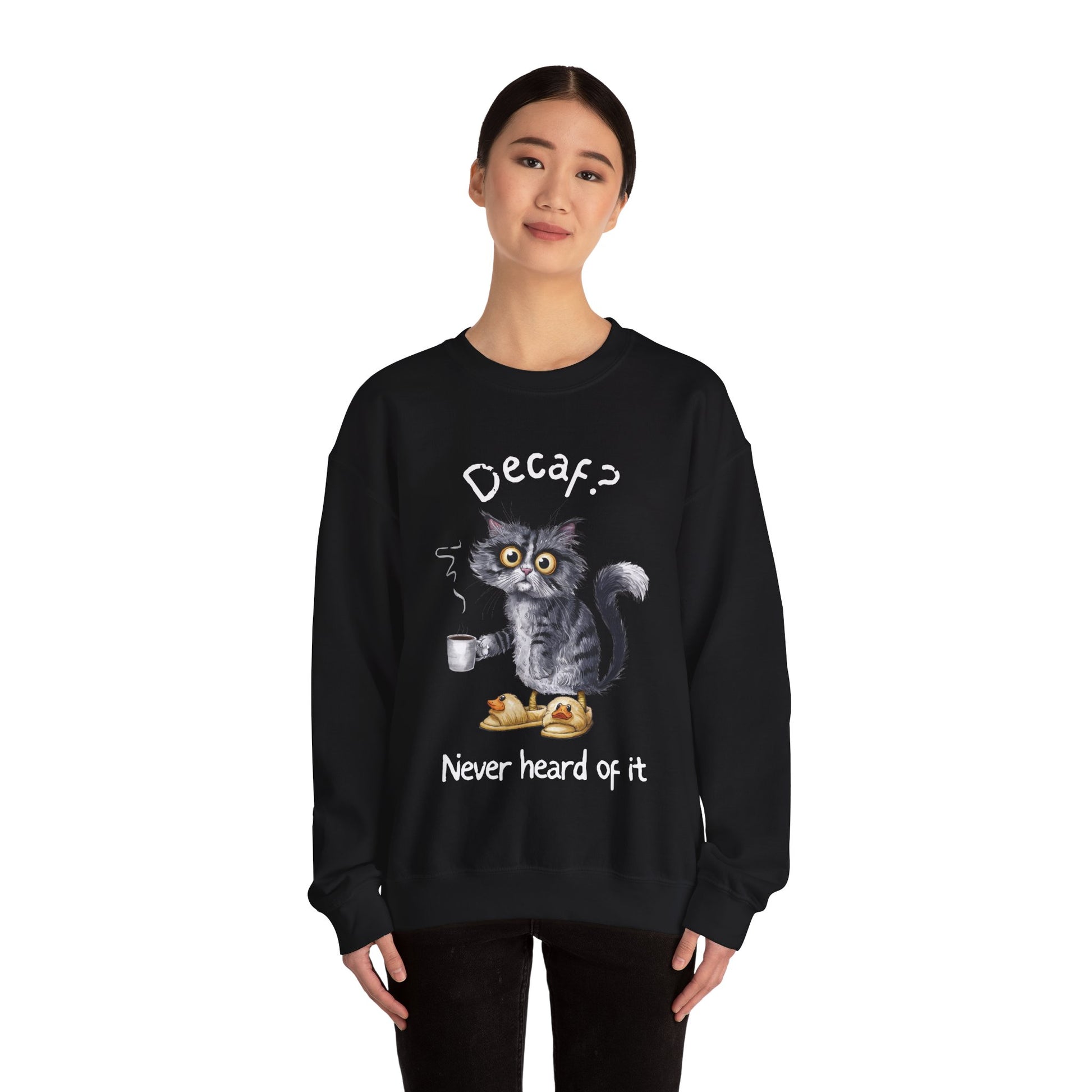 A sweatshirt featuring an exhausted-looking cat wearing yellow slippers with duck faces on them. The cat is holding a steaming mug of coffee. The text on the sweatshirt reads "Decaf? Never Heard of It."