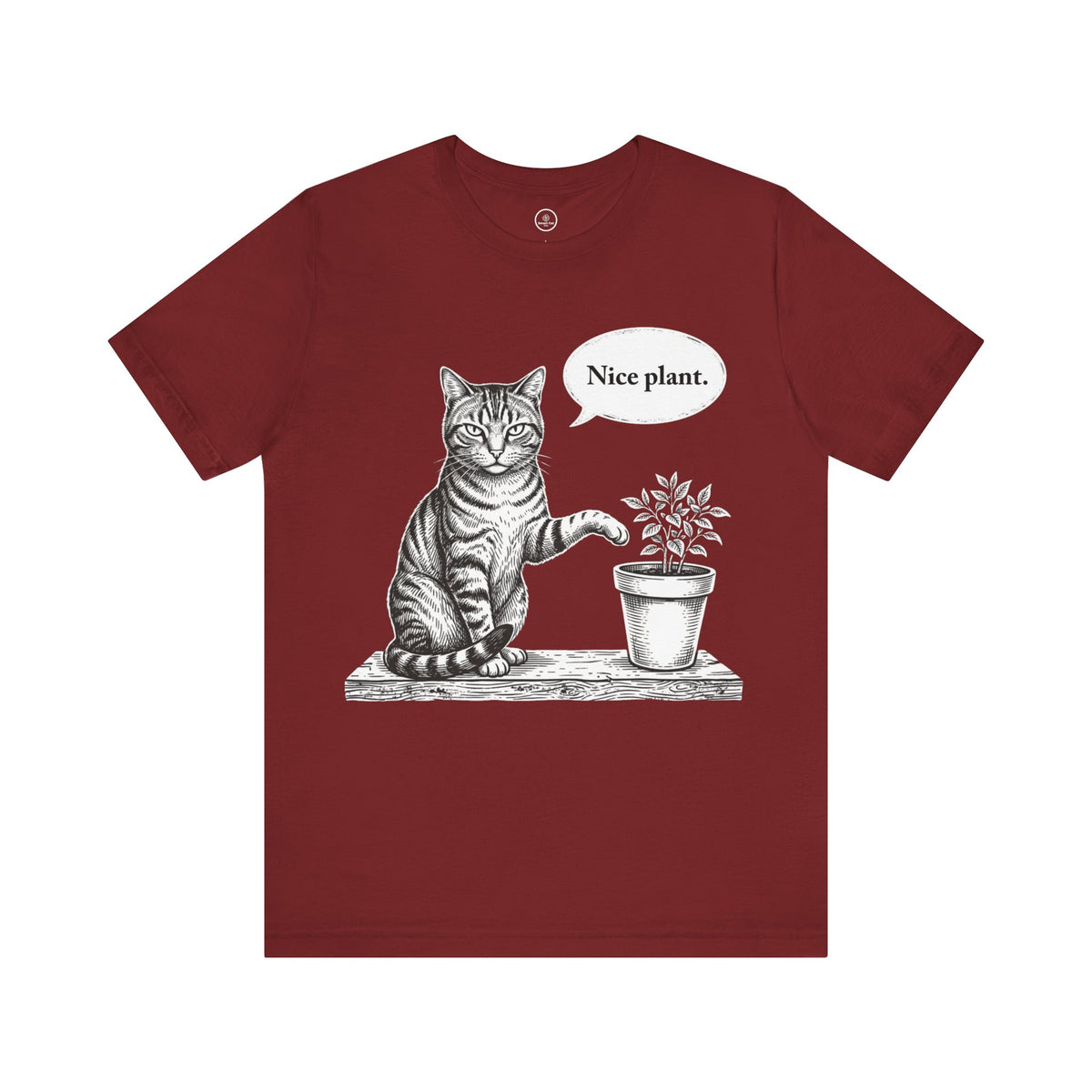 A cardinal red short-sleeve crewneck t-shirt featuring a black and white sketch of a cat sitting next to a potted plant with a speech bubble that says 'Nice plant.' on a plain white background.