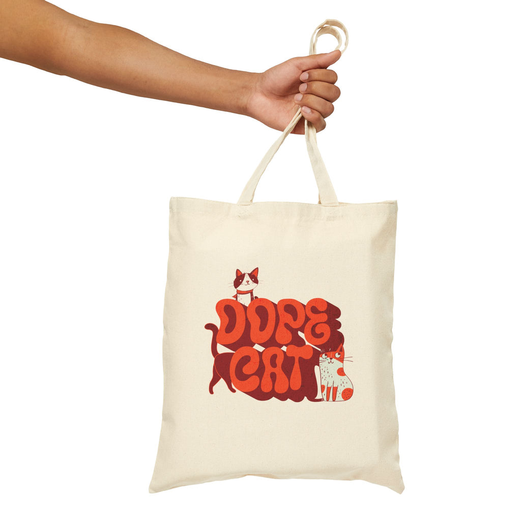 Person holding a beige tote bag with red and white 'Dope Cat' text and cat graphics