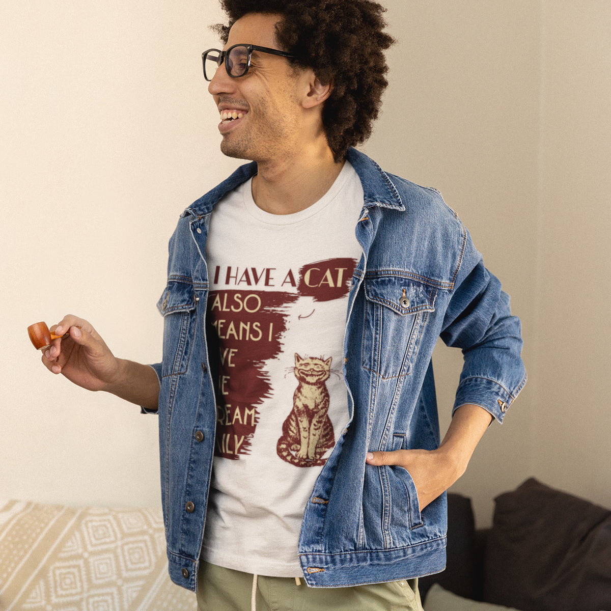 A man wearing a white graphic t-shirt with a cat design and text, layered under a blue denim jacket, standing in a casual indoor setting.