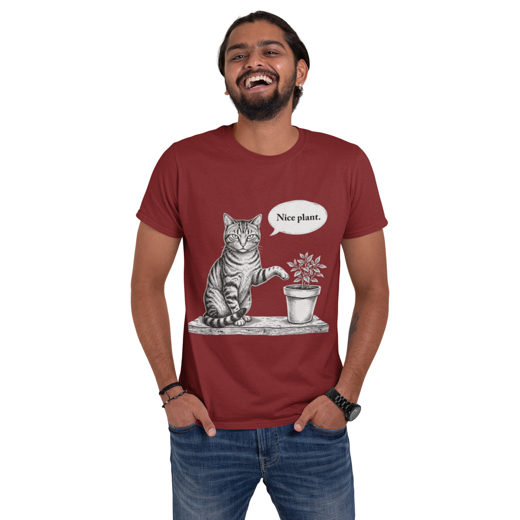 A man wearing a red crewneck t-shirt with a graphic of a cat sitting next to a potted plant and a speech bubble that says 'Nice plant.' He is posing with his hands in his pockets against a plain white background.