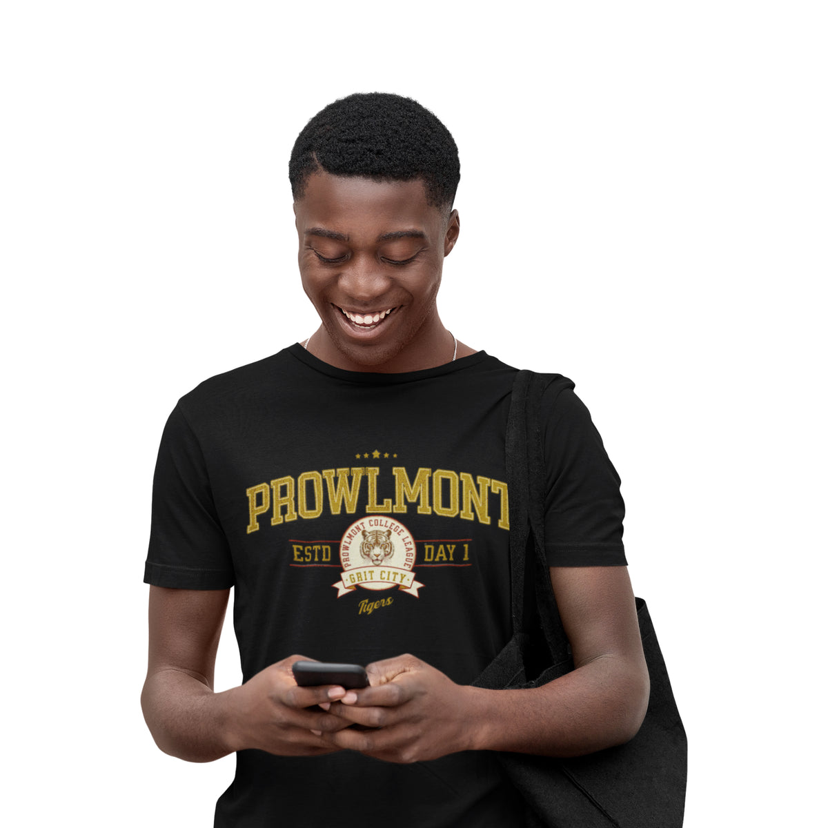 A smiling young man looking down at a phone he is holding, wearing a black crewneck t-shirt with yellow and white 'PROWLMONT Grit City tigers Text