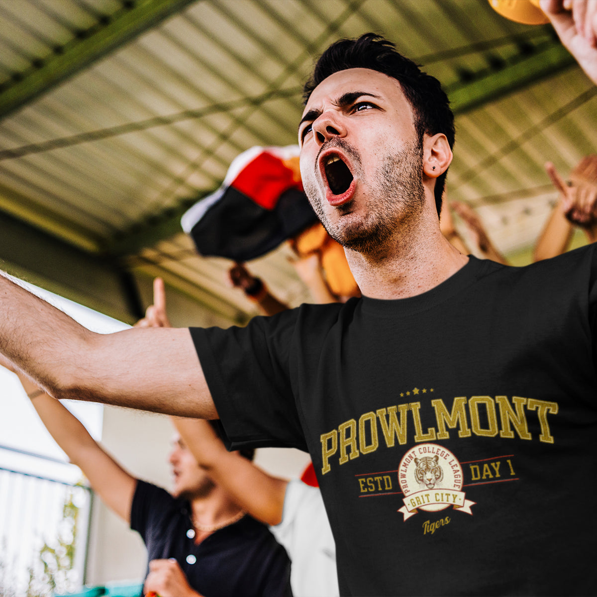 A man at a sporting event wearing a black Prowlmont Grit City Tigers T-Shirt