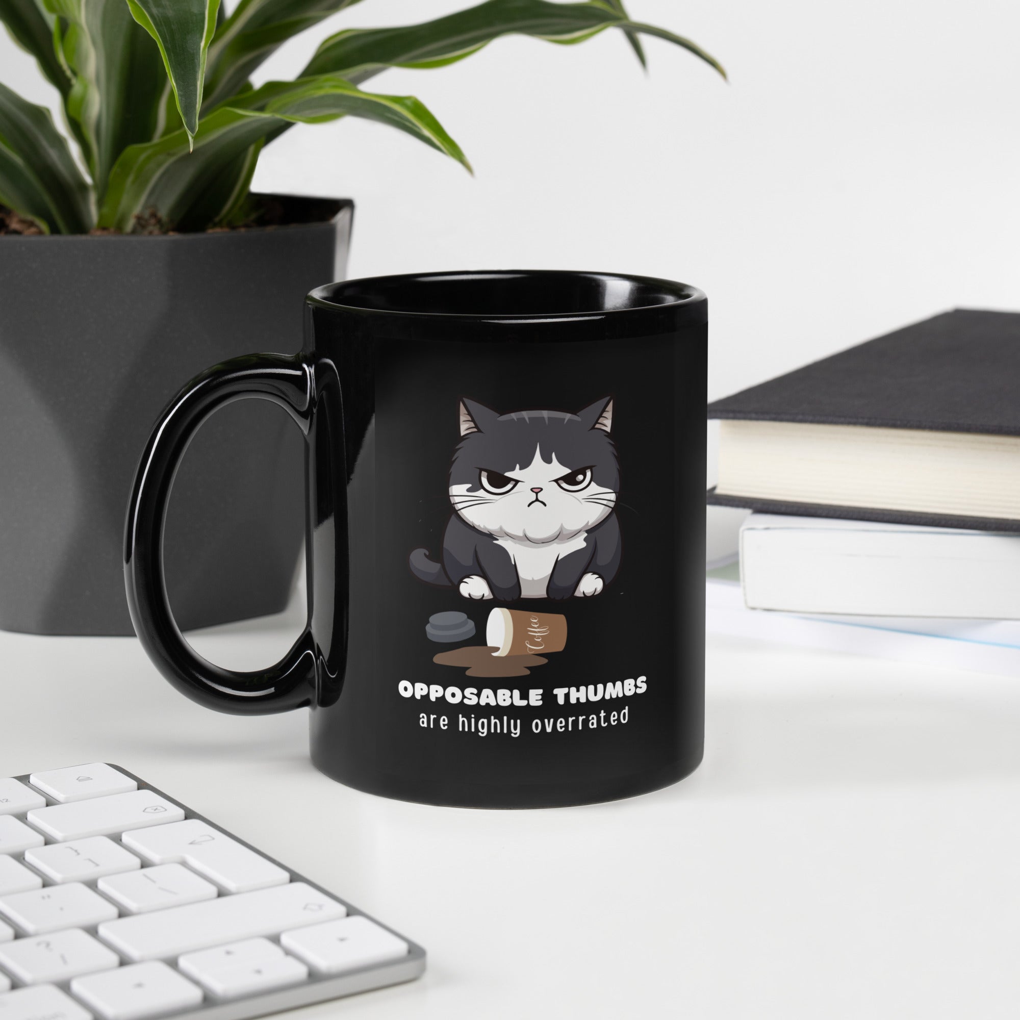 Black glossy mug with a graphic of a frustrated cartoon cat standing over spilled coffee. Text below the cat reads "Opposable Thumbs Are Highly Overrated".