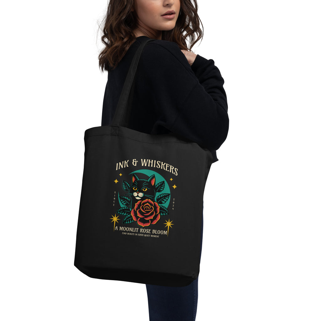 Black tote bag with a cat and rose design on the cover, featuring the text 'Ink & Whiskers'.