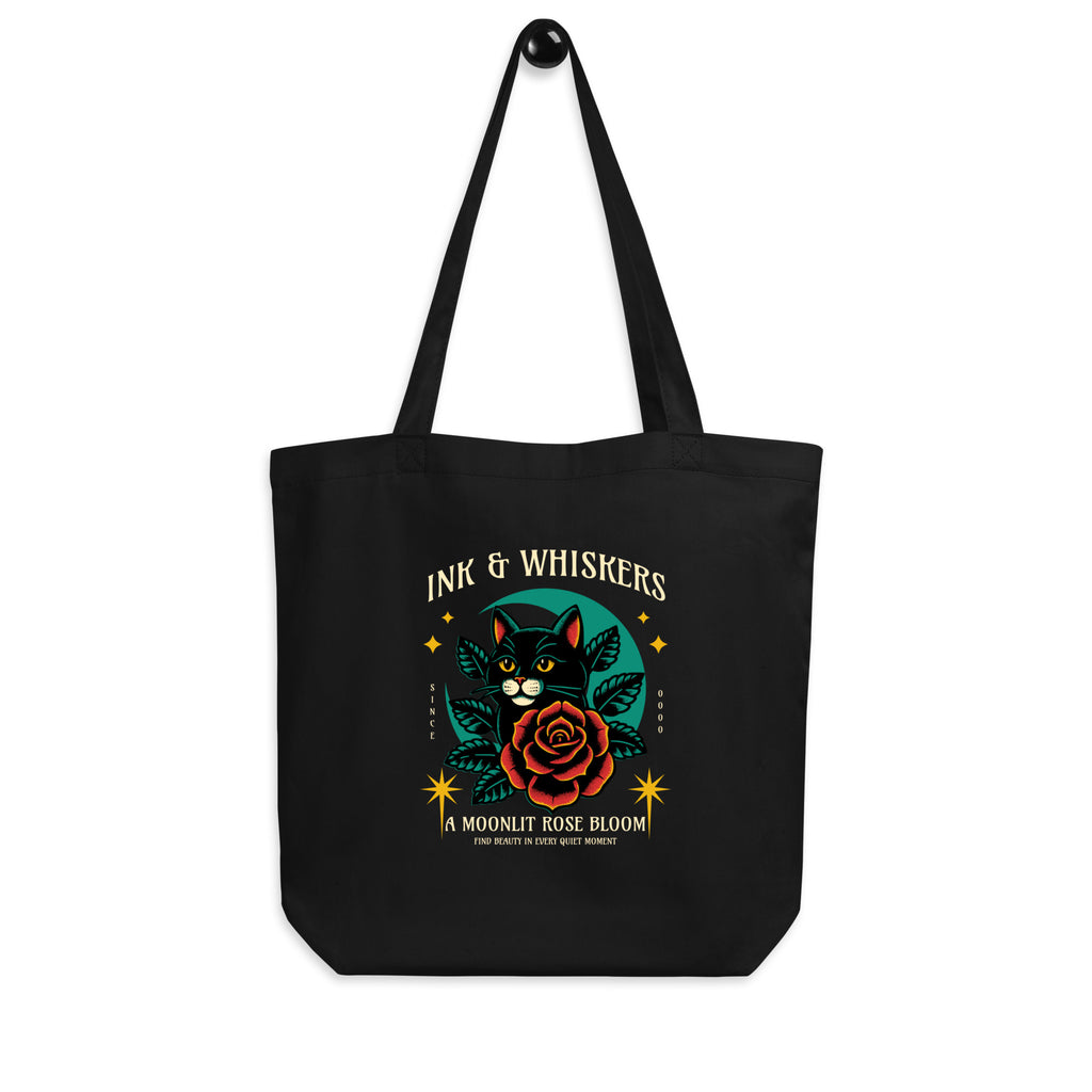 Black tote bag with a cat and rose design on the cover, featuring the text 'Ink & Whiskers'.