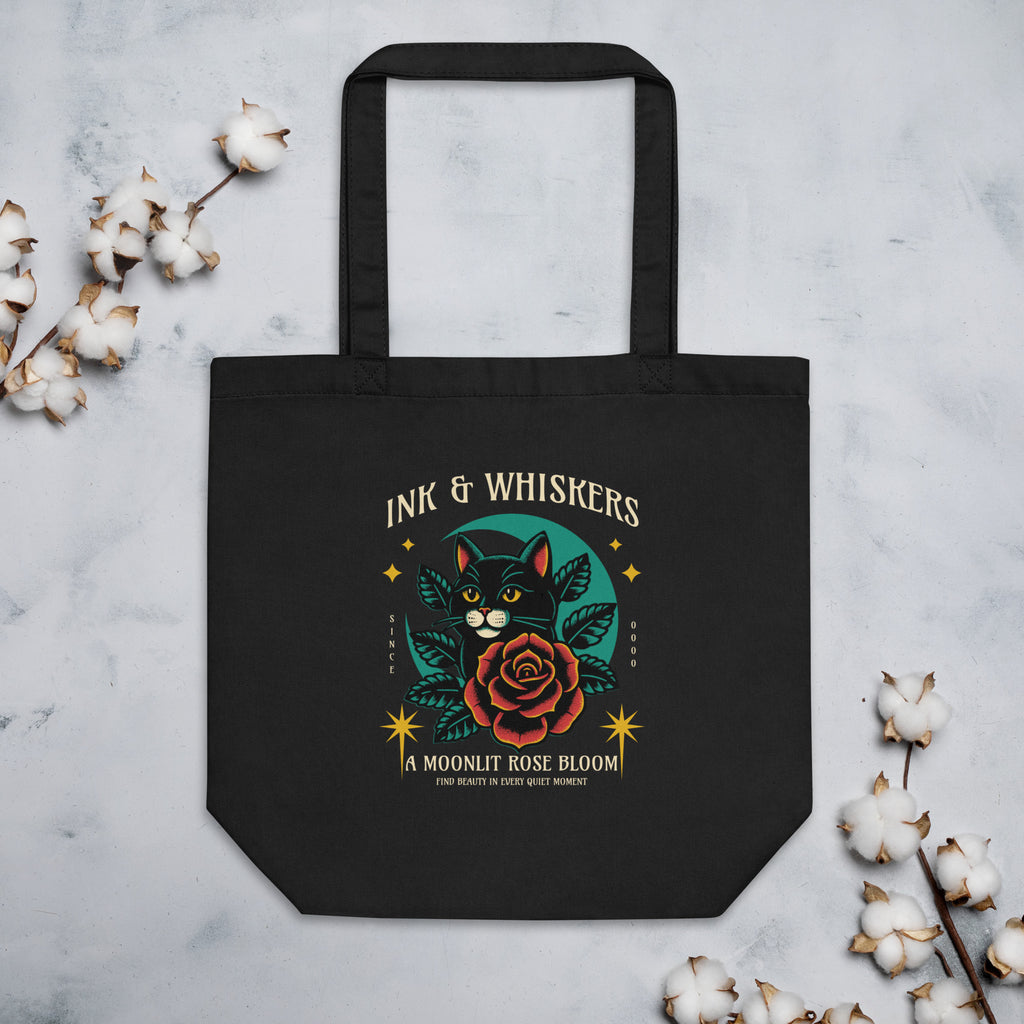 Black tote bag with a cat and rose design on the cover, featuring the text 'Ink & Whiskers'.