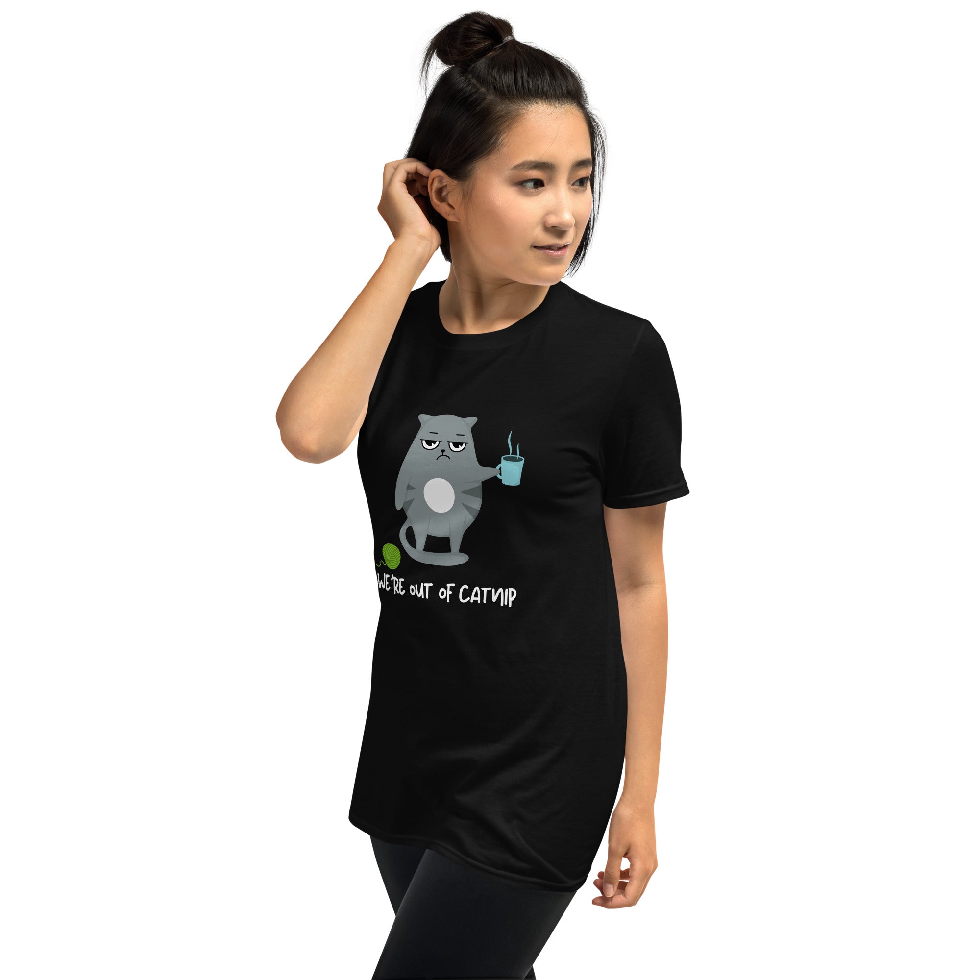 Crewneck t-shirt featuring a cartoon gray and white cat smugly holds a steaming cup of coffee. A green ball of yarn sits on the floor nearby. Below the image, the text reads "We're Out Of Catnip".