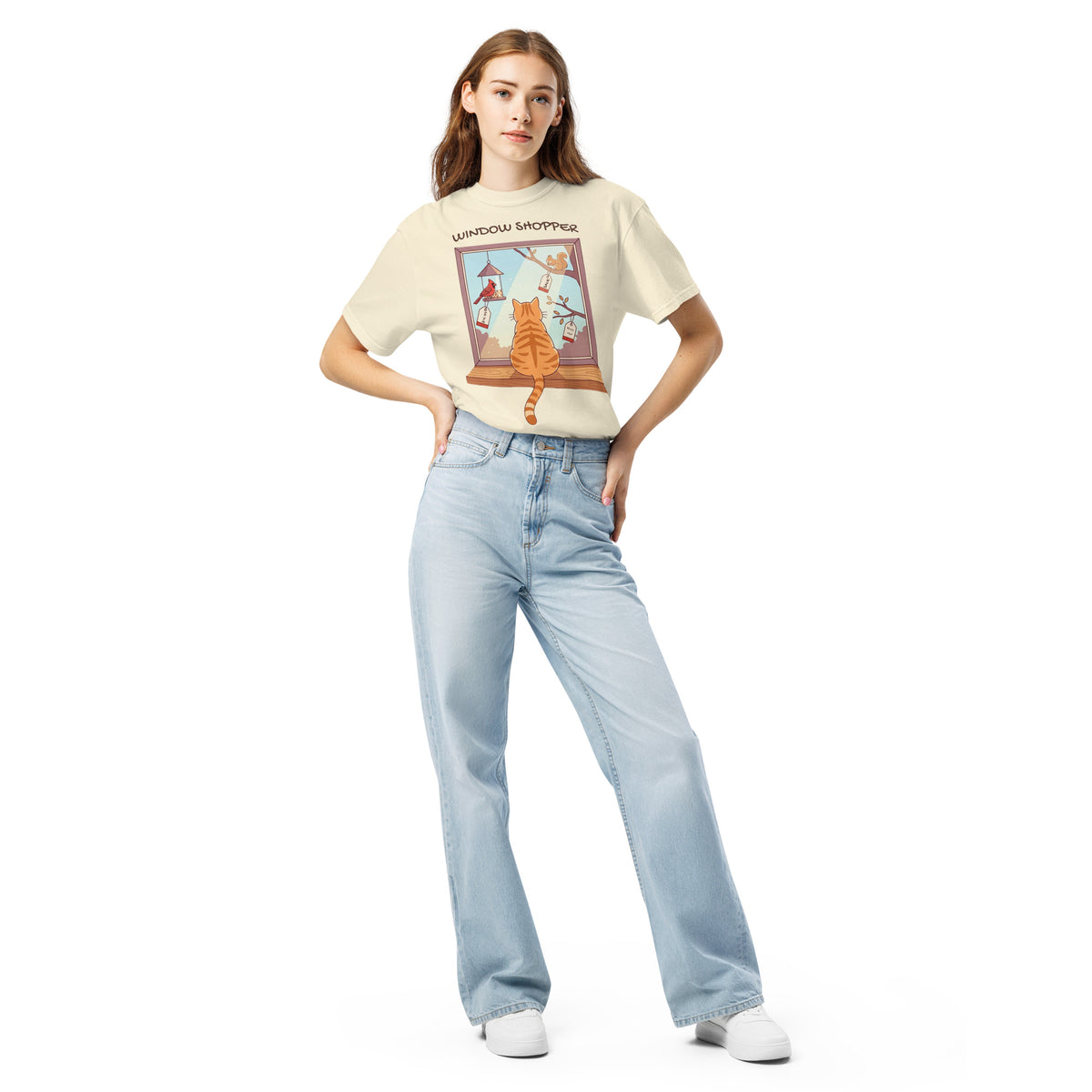 A model wearing the Ivory Window Shopper tee tucked into jeans, orange cat at a window graphic