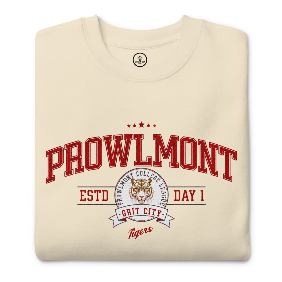 A folded cream-colored t-shirt with a red and white graphic print on the front reading 'PROWLMONT ESTD DAY 1 GRIT CITY Tigers' with a tiger mascot logo.