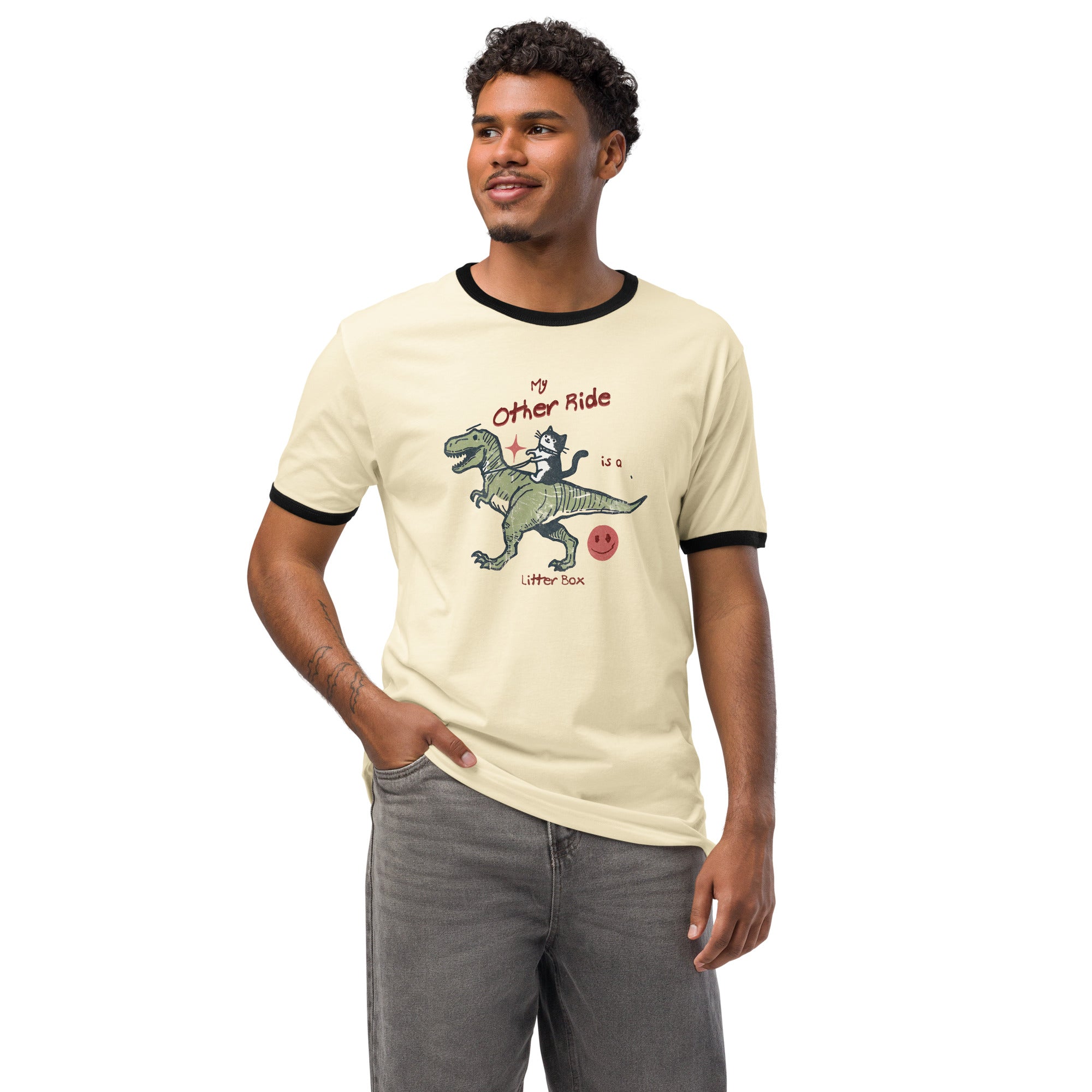 Beige ringer t-shirt with a cat riding a dinosaur  graphic. The text reads 'My other ride is a litter box'.