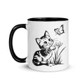 A white and black mug featuring a line art design of a playful encounter between a curious kitten and a gentle butterfly